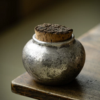 Small ceramic silver metallic pet urn with cork lid on a wooden surface combining unique craftmanship with modern design