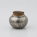 Small ceramic silver metallic pet urn with cork lid on a wooden surface combining unique craftmanship with modern design
