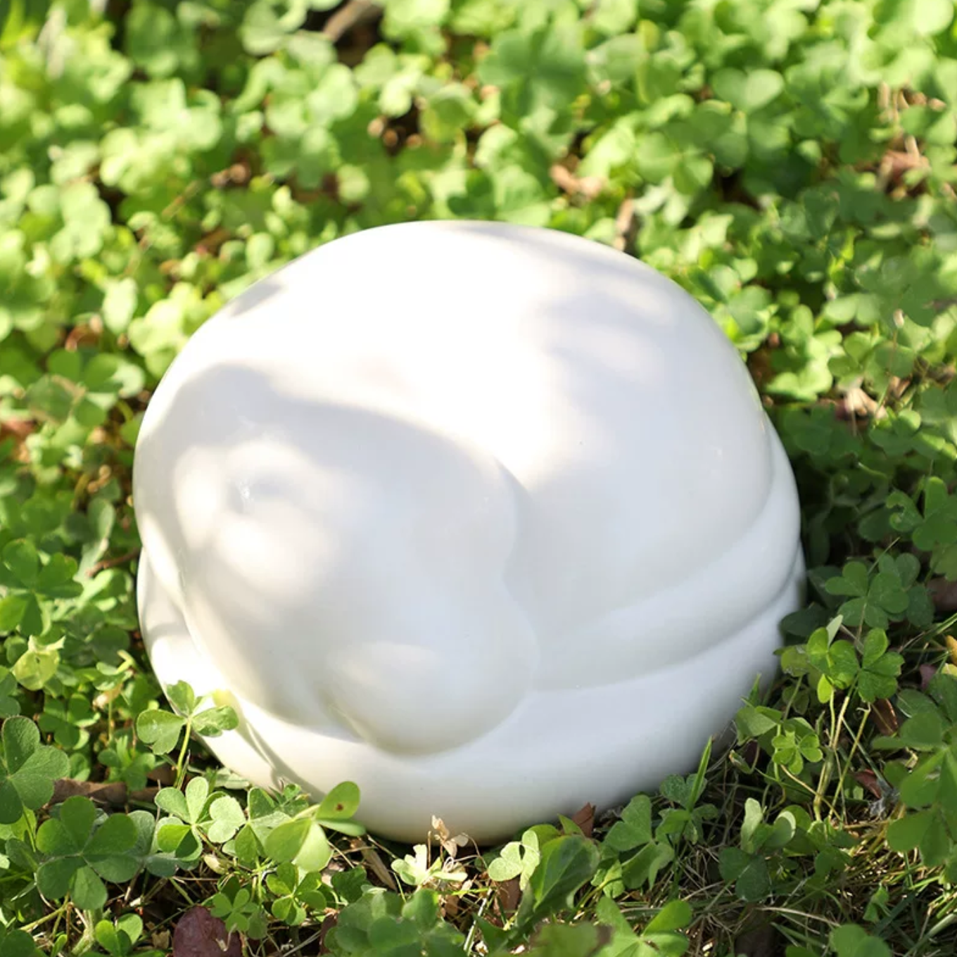 Satin white porcelain ceramic urn sculpture of a sleeping dog outside
