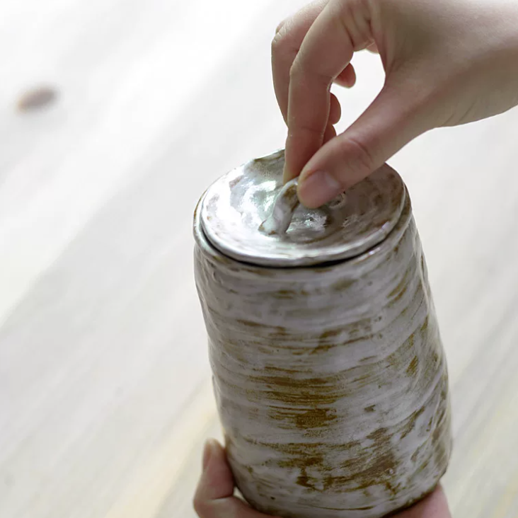 Hand holding glazed white brown artisanal pet urn with organic shape and color patterns